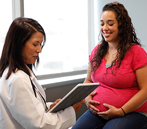 Pregnant woman sitting on exam table, talking to doctor.